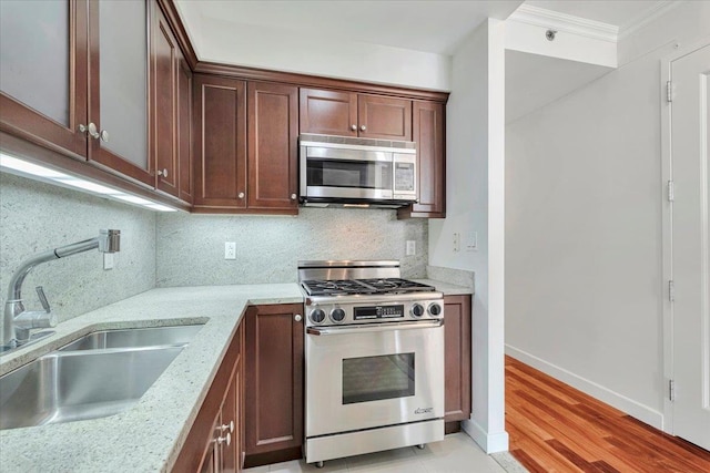 kitchen with sink, tasteful backsplash, ornamental molding, stainless steel appliances, and light stone countertops