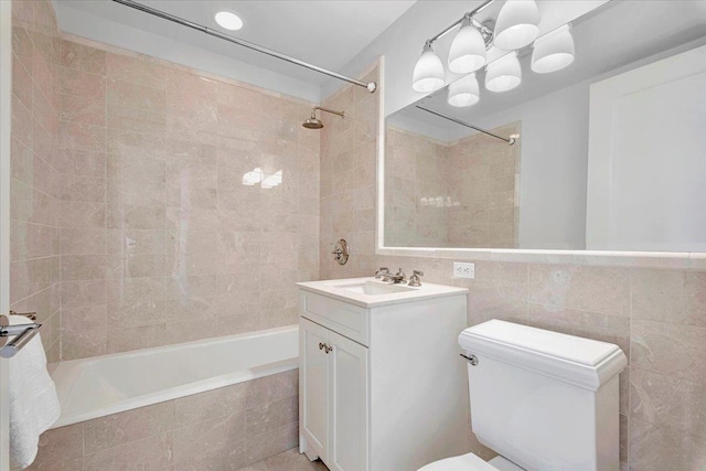 full bathroom with tiled shower / bath, vanity, toilet, and tile walls