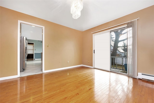 spare room featuring a baseboard radiator, an inviting chandelier, and light hardwood / wood-style floors