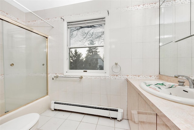 full bathroom featuring bath / shower combo with glass door, vanity, a baseboard heating unit, tile walls, and tile patterned flooring