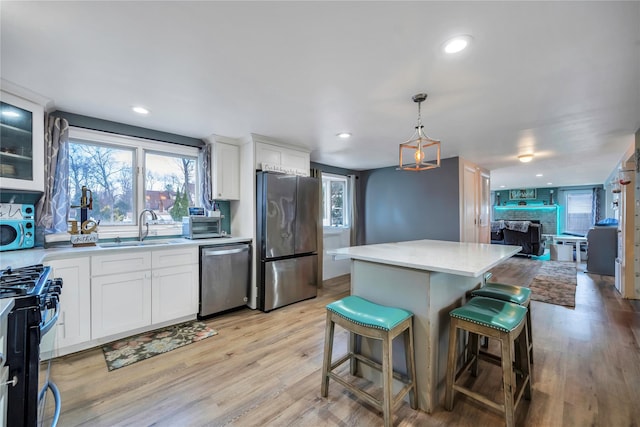 kitchen with appliances with stainless steel finishes, sink, white cabinets, a center island, and light hardwood / wood-style floors