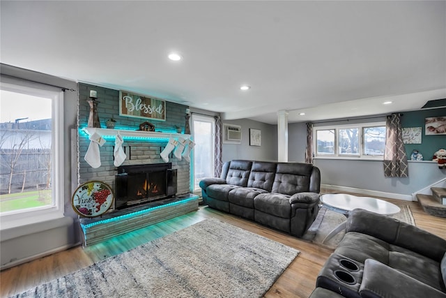 living room featuring wood-type flooring, a brick fireplace, and a healthy amount of sunlight