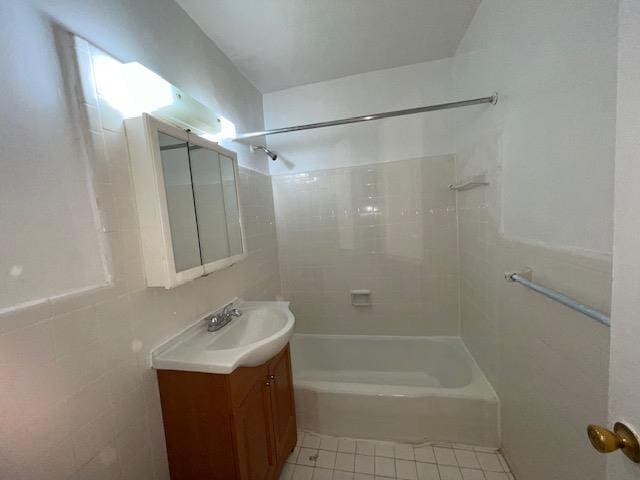 bathroom with tile patterned flooring, tile walls, vanity, and tiled shower / bath combo