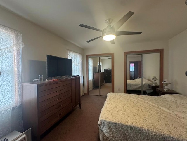 bedroom with dark colored carpet, two closets, and ceiling fan