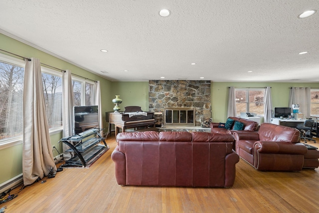 living room with light hardwood / wood-style floors, a textured ceiling, and a stone fireplace