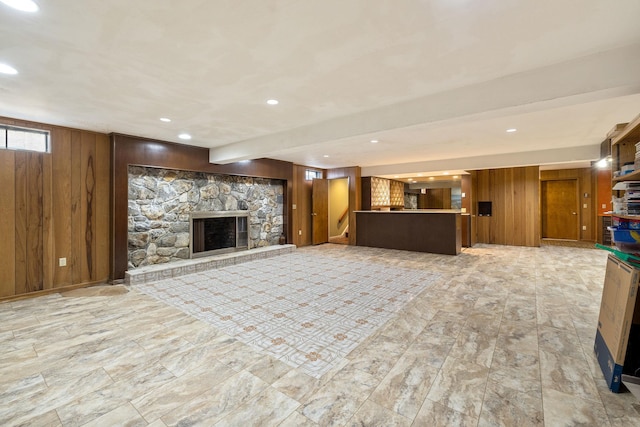 unfurnished living room featuring beamed ceiling, wood walls, and a stone fireplace