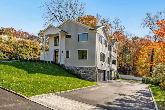neoclassical home with stairway, aphalt driveway, stone siding, a front yard, and an attached garage
