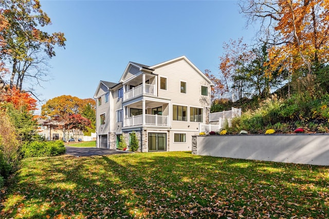 view of home's exterior with a balcony, a yard, stone siding, aphalt driveway, and an attached garage