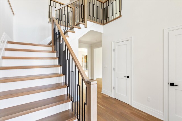 stairs featuring a towering ceiling, wood finished floors, and baseboards