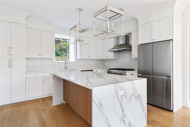 kitchen featuring an inviting chandelier, a sink, a center island, wall chimney exhaust hood, and stainless steel refrigerator