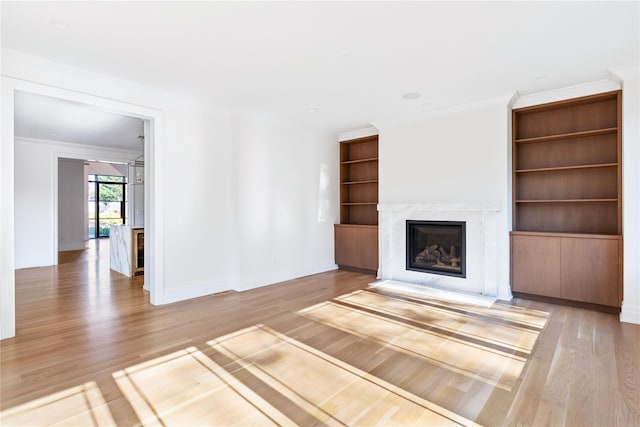 unfurnished living room featuring a fireplace with flush hearth, light wood-style floors, built in shelves, and baseboards