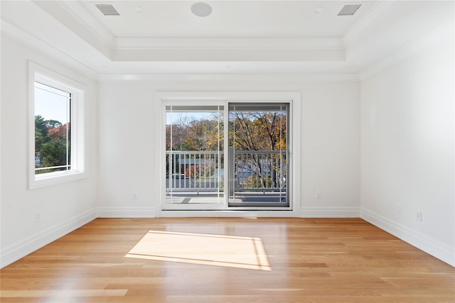 empty room with a raised ceiling, plenty of natural light, visible vents, and crown molding