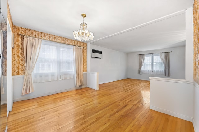 unfurnished room featuring light hardwood / wood-style floors, a wall mounted AC, and a notable chandelier