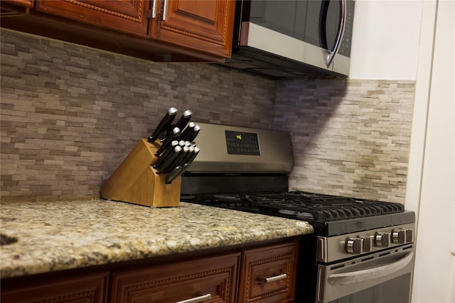 kitchen with backsplash, light stone counters, and stainless steel appliances