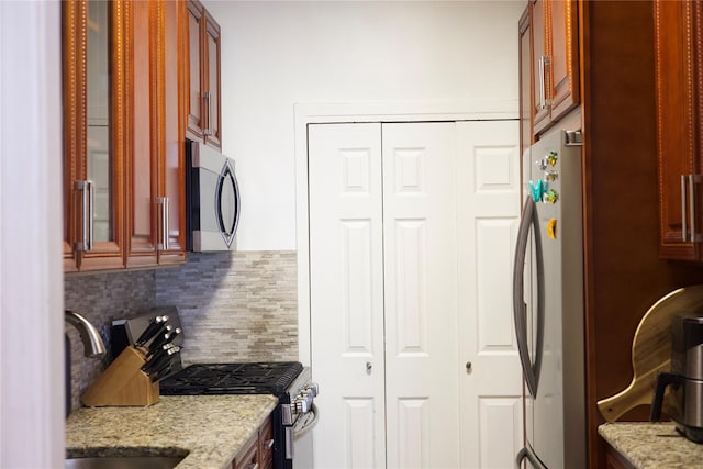 kitchen featuring appliances with stainless steel finishes, backsplash, light stone counters, and sink