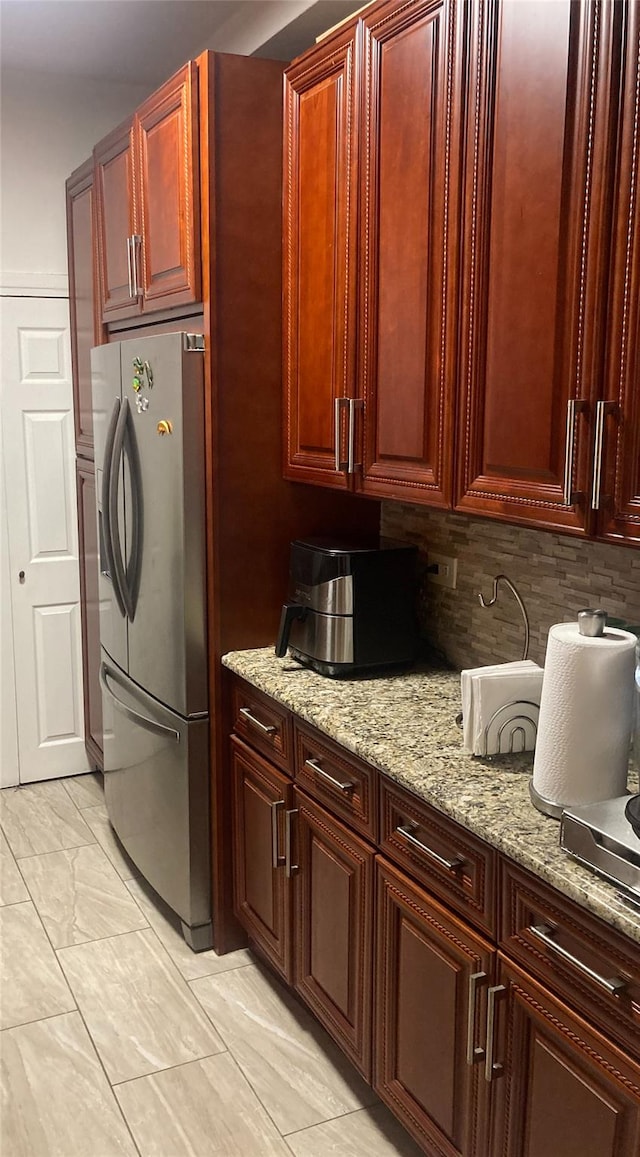 kitchen featuring light stone countertops, stainless steel fridge, and decorative backsplash