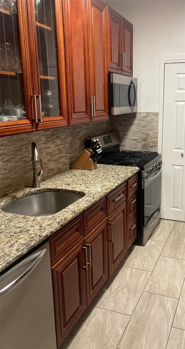 kitchen with backsplash, light stone countertops, sink, and appliances with stainless steel finishes