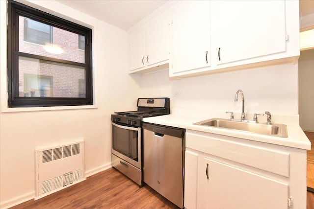 kitchen with white cabinets, sink, hardwood / wood-style flooring, appliances with stainless steel finishes, and radiator heating unit