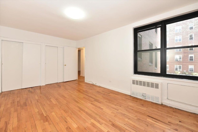 unfurnished bedroom with radiator, light hardwood / wood-style flooring, and two closets