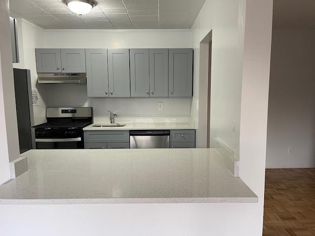 kitchen with dark parquet floors, sink, gray cabinets, range hood, and appliances with stainless steel finishes