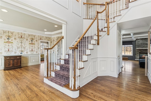 stairway featuring wood-type flooring, a stone fireplace, crown molding, and coffered ceiling