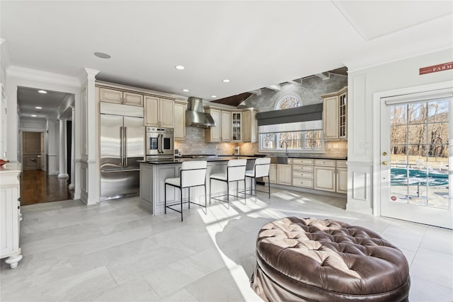 kitchen featuring a wealth of natural light, stainless steel appliances, wall chimney range hood, a kitchen bar, and a kitchen island