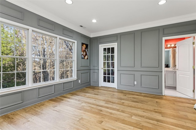 spare room featuring plenty of natural light, light wood-type flooring, and ornamental molding