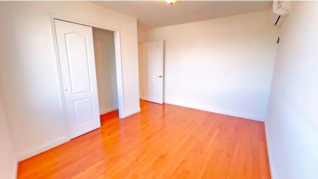 unfurnished bedroom with wood-type flooring, an AC wall unit, and a closet