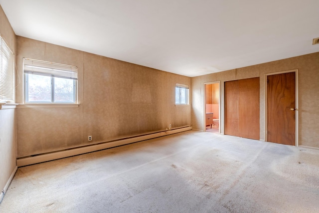 unfurnished bedroom featuring baseboard heating, connected bathroom, light colored carpet, and two closets