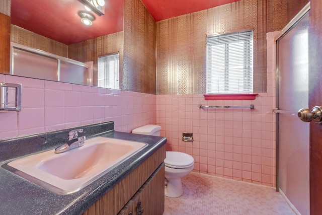 bathroom featuring tile patterned floors, toilet, vanity, a shower with shower door, and tile walls