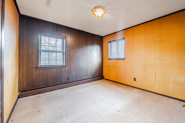 empty room with wood walls, ornamental molding, light carpet, and a baseboard heating unit