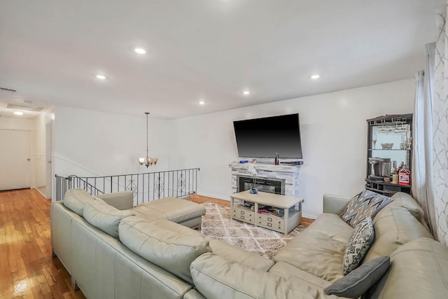 living room featuring a stone fireplace, a chandelier, and light wood-type flooring