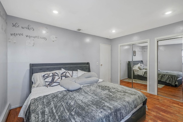 bedroom featuring hardwood / wood-style floors, two closets, and a baseboard heating unit