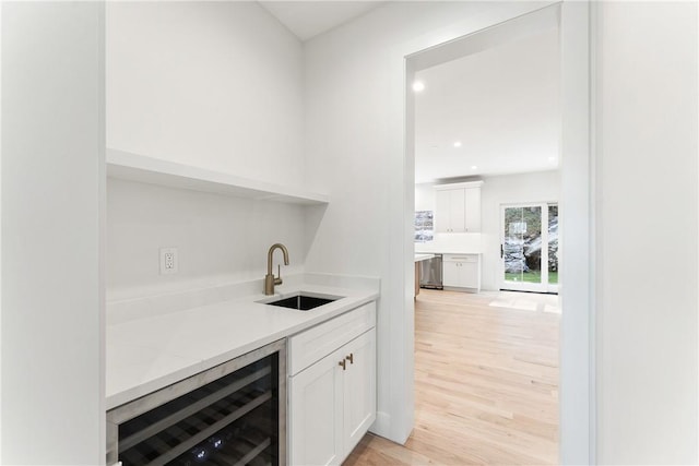 bar with white cabinetry, sink, wine cooler, light stone counters, and light wood-type flooring