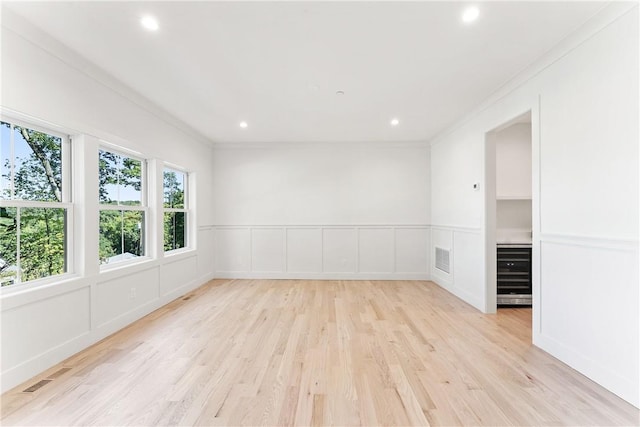 empty room featuring crown molding, beverage cooler, and light wood-type flooring