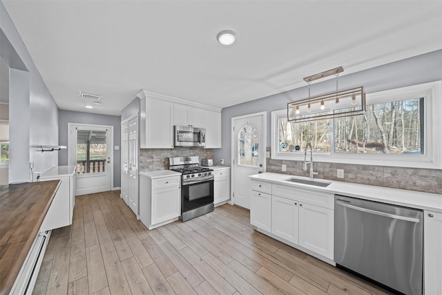 kitchen with butcher block counters, sink, decorative light fixtures, white cabinetry, and stainless steel appliances