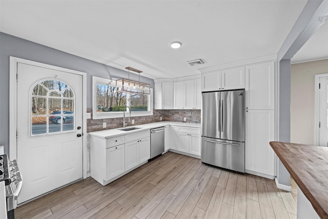 kitchen featuring stainless steel appliances, sink, white cabinets, butcher block countertops, and hanging light fixtures