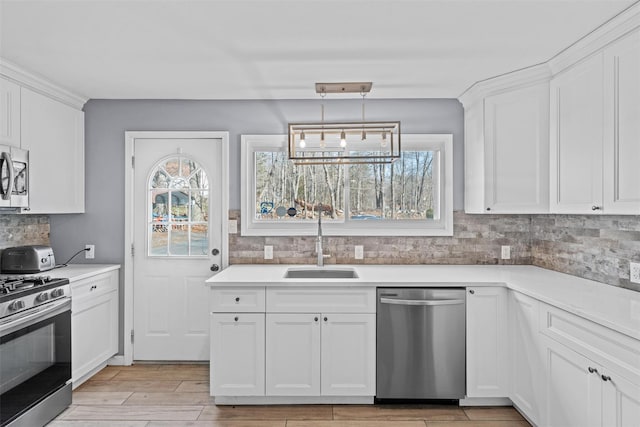 kitchen with white cabinetry, sink, stainless steel appliances, and decorative light fixtures