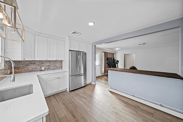 kitchen featuring a baseboard heating unit, sink, tasteful backsplash, white cabinetry, and stainless steel refrigerator