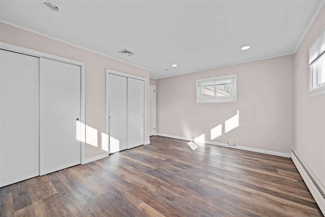 unfurnished bedroom featuring multiple windows, dark wood-type flooring, baseboard heating, and multiple closets