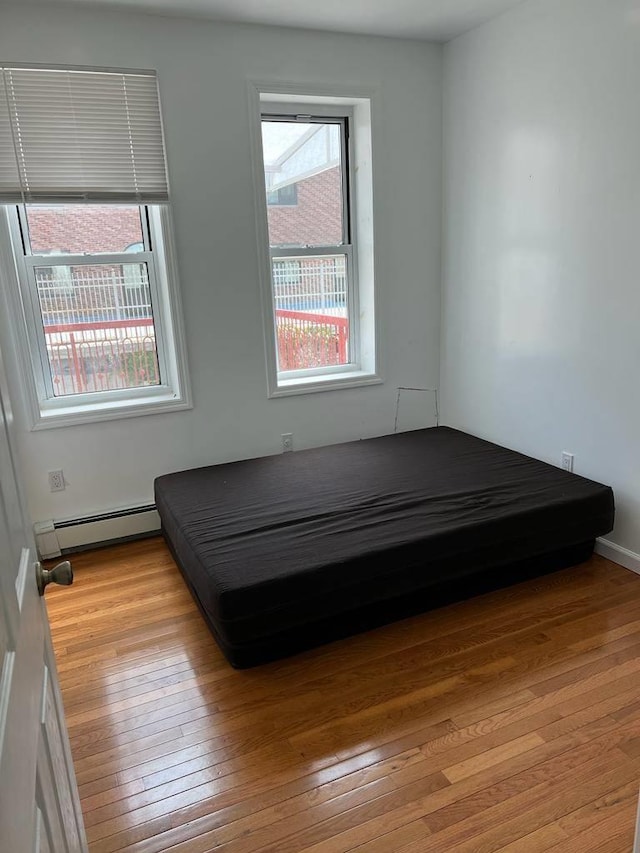 unfurnished bedroom with light hardwood / wood-style floors and a baseboard heating unit