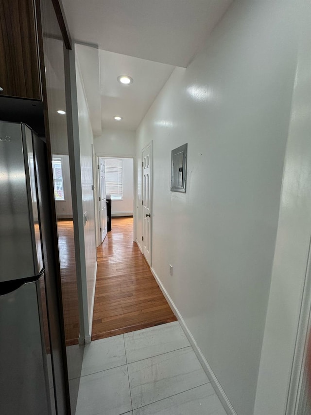 corridor with light wood finished floors, baseboards, electric panel, and recessed lighting