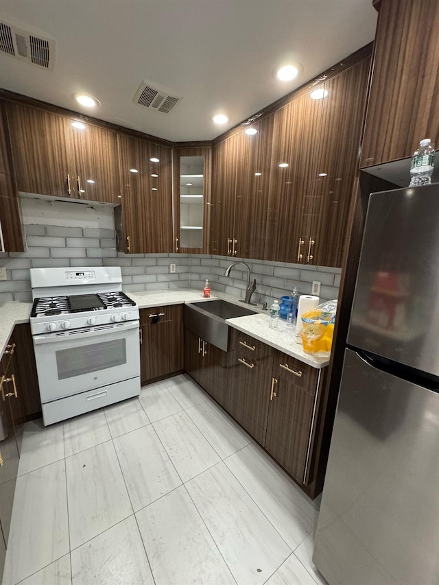 kitchen with a sink, freestanding refrigerator, white gas range oven, and visible vents