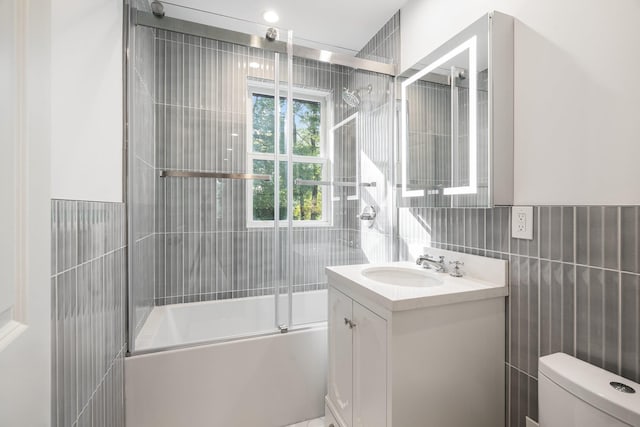 full bathroom with tile walls, vanity, shower / bath combination with glass door, and toilet