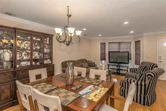 dining room with an inviting chandelier, light wood-type flooring, and crown molding