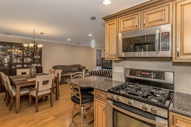 kitchen with an inviting chandelier, stainless steel appliances, crown molding, dark stone counters, and decorative light fixtures