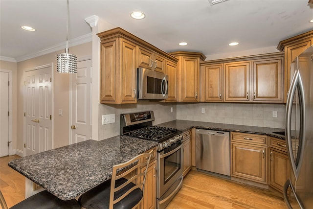 kitchen featuring a kitchen breakfast bar, appliances with stainless steel finishes, hanging light fixtures, light wood-type flooring, and tasteful backsplash