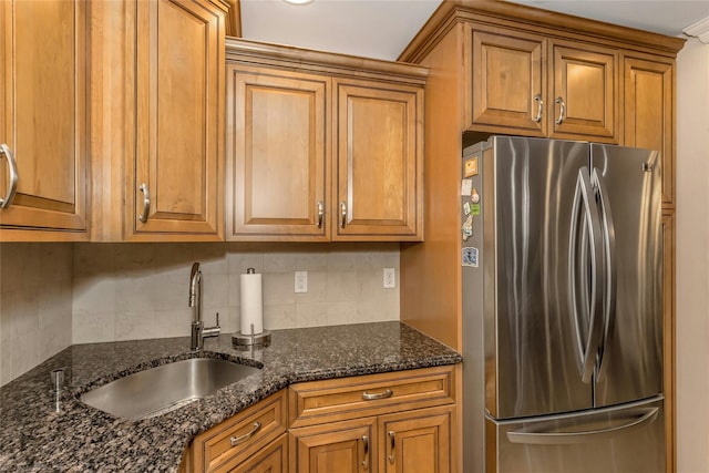 kitchen with dark stone counters, stainless steel fridge, tasteful backsplash, and sink