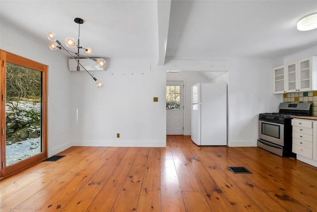 kitchen featuring beam ceiling, gas range, white cabinetry, white refrigerator, and decorative light fixtures