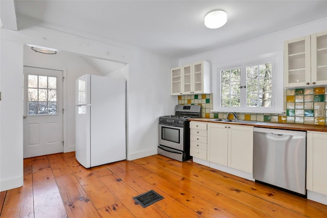 kitchen featuring white cabinetry, sink, stainless steel appliances, light hardwood / wood-style flooring, and backsplash